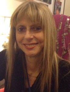 Stephanie Dickinson smiles at the camera. She has long, straight,  blond hair with bangs, and she wears a dark shirt with a v neck. 