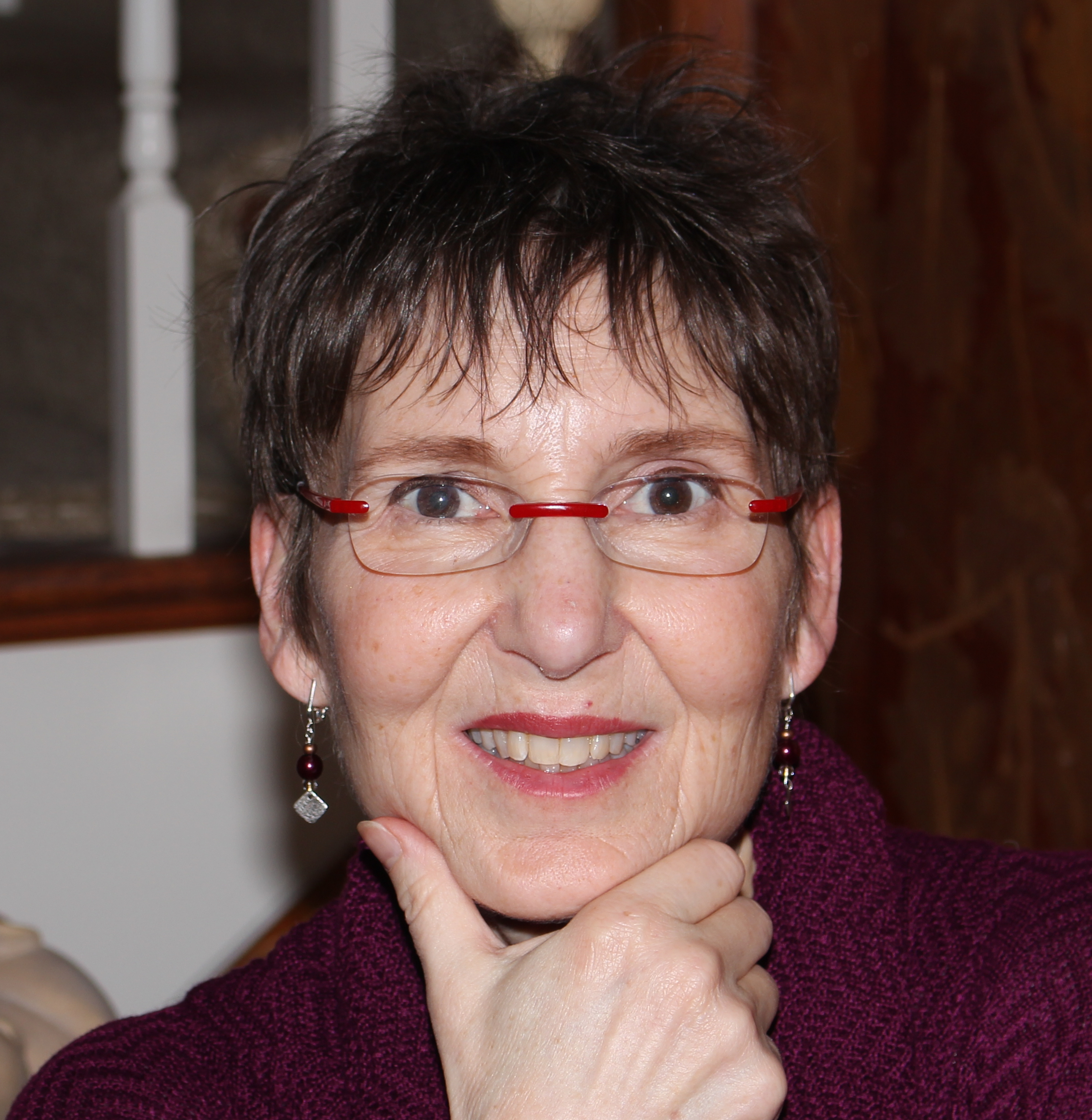 Michele Ruby rests her head in one hand and smiles at the camera. She has short dark hair and wire frame glasses, and wears a burgundy sweater. 