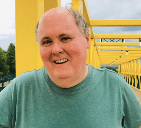 Garin Cycholl, smiling, in a green shirt on a yellow bridge