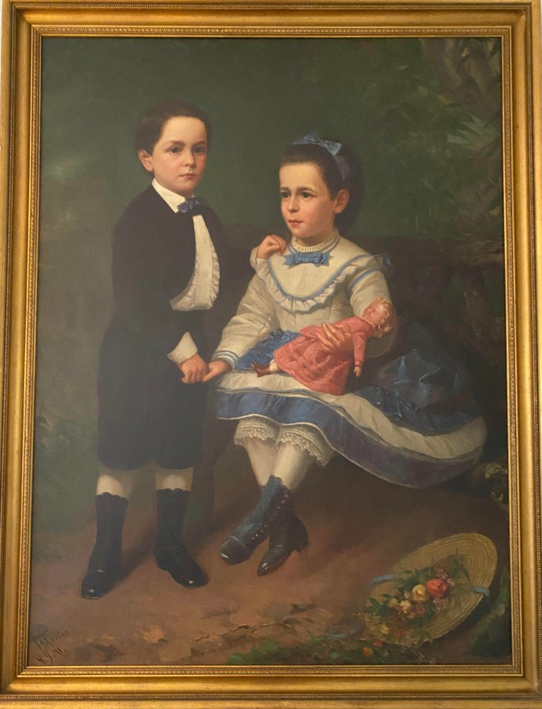 Twin children in the woods. They are dressed formally. The painting is in a gold frame.