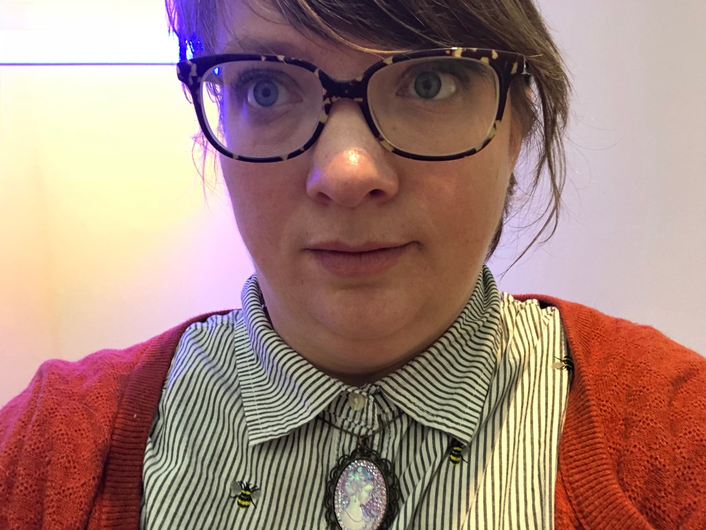 Author photo: Rebecca Hamlin has large glasses, smooth brown hair and wears a button down, cardigan and cameo necklace.