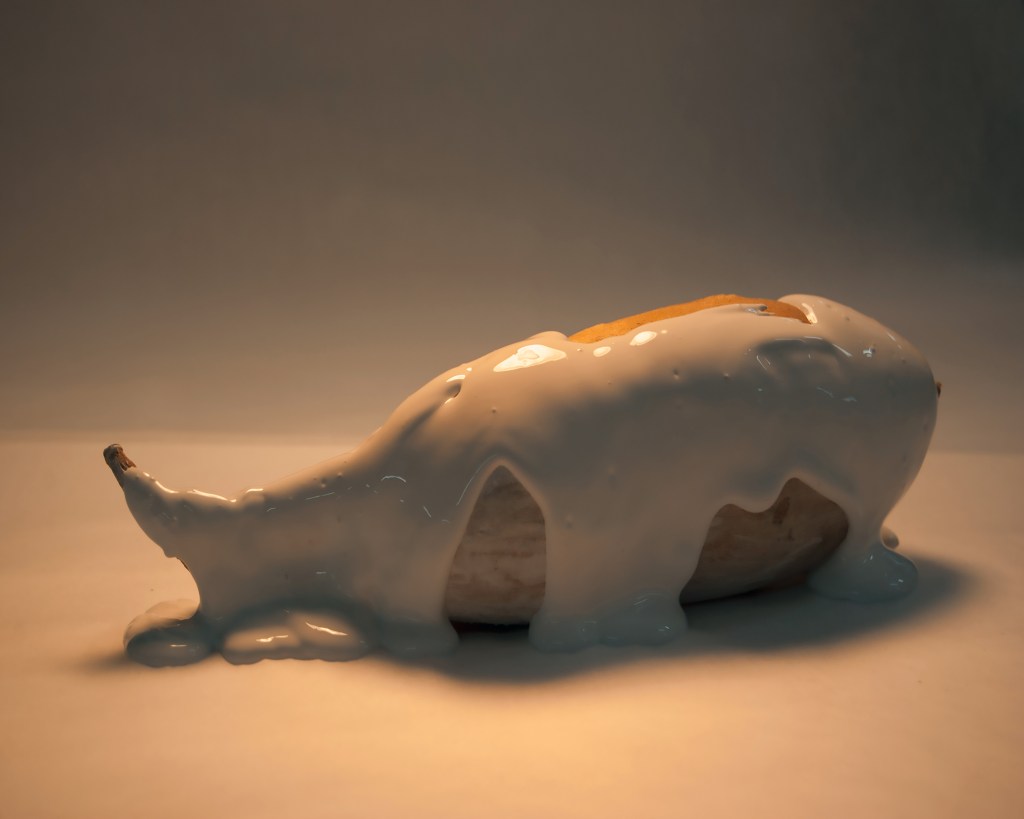 A majestic sweet potato slathered in viscous opaque fluid gleams in low yellow light against a gray fading background