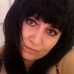 Irina has long black hair and thick bangs that hang just over her eyebrows. Her head is titled and she's looking into the camera.