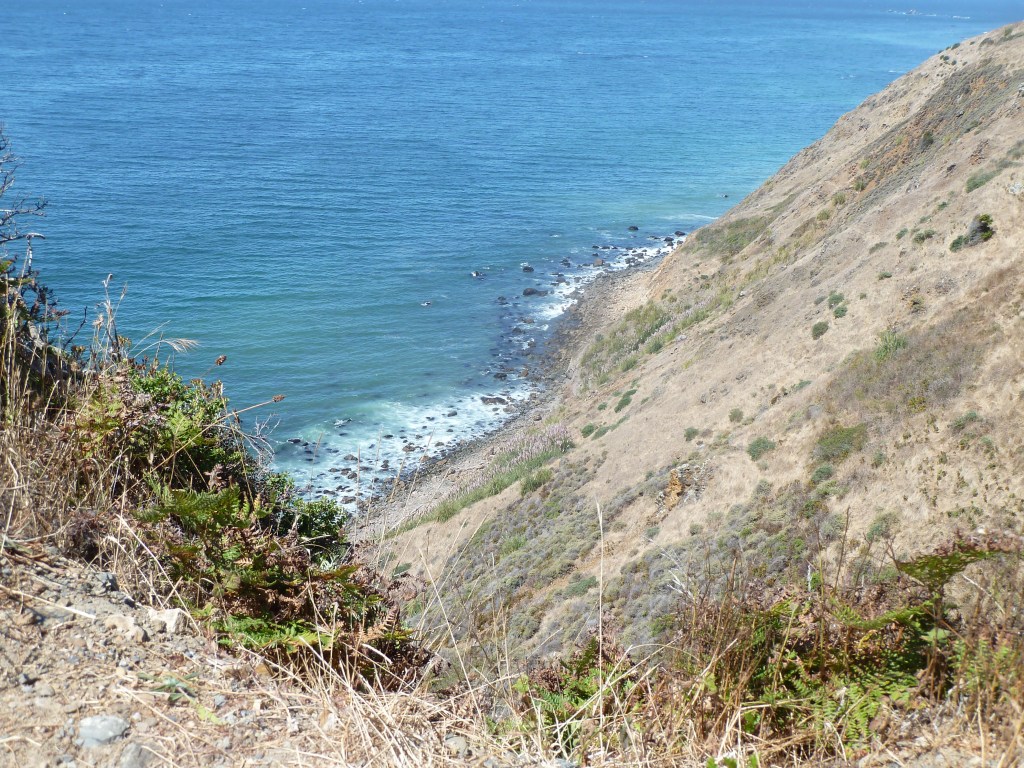 A very blue ocean behind hills. The hills are mainly brown, the grass hasn't grown.