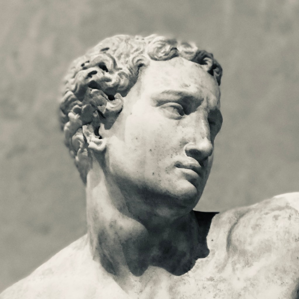 Marble statue of Alpheus. Shoulders and head visible. Muscular face and shoulders. The statue is looking to the right and has a sad expression.
