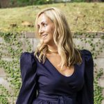 Elisabetta is wearing a dark blue long sleeve blouse. She is smiling and her head is turned to the left. She has long blonde hair.