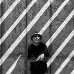 Jeff is wearing a hat and black sunglasses. He is leaning against a wall. Diagonal white stripes fill the photo.