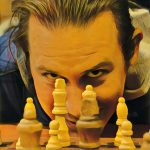 Photo of Charles J. March III. He is leaning down in front of a chess board. Most of his face is covered by the chess pieces. He has short brown hair.