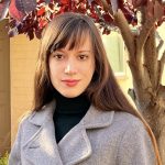 Photo of Jury S. Judge. She has long brown hair and bangs. She is wearing a black turtleneck and a gray peacoat.