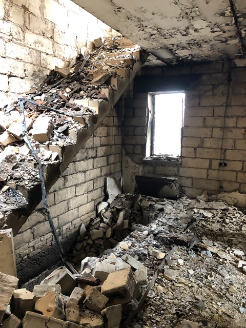 Another photo of Irpin by Victor G. This cinderblock interior has a crumbling stairway that leads to a collapsed second floor, filled with bright sunlight (no roof anymore). The blown out window below sheds light on pulverized bricks. 