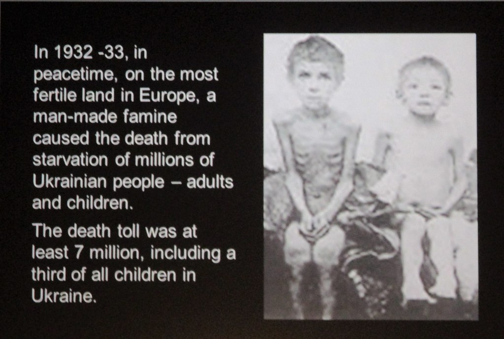 An original photo by Wienenberger or Dr. Fritz Dittloff, provided by Diego Sideburns. It is a photograph of two children, one emaciated, with bones and ribs showing. To the left, a block of text on a black background reading "In 1932-33, in peacetime, on the most fertile land in Europe, a man-made famine caused the death from starvation of millions of Ukrainian people - adults and children. The death toll was at least 7 million, including a third of all children in Ukraine. "