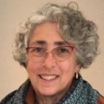 Photo of Susanna Lang. She has short, curly gray hair. She wears red glasses.