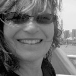 Author photo: a black and white closeup of Suzanne Jill Levine, wearing sunglasses and smiling at the camera, her bangs glinting in the sun. 